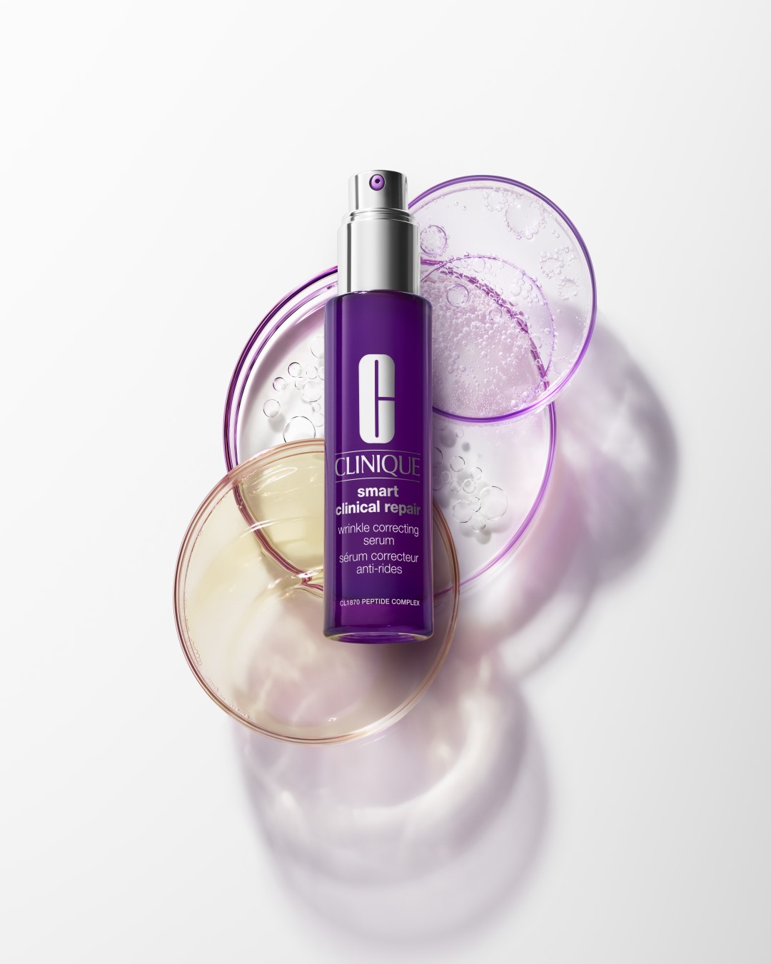 Fioletowa butelka serum Clinique Smart Clinical Repair otoczona szklanymi naczyniami laboratoryjnymi, obiecująca korekcję zmarszczek dzięki kompleksowi peptydowemu CL1870.