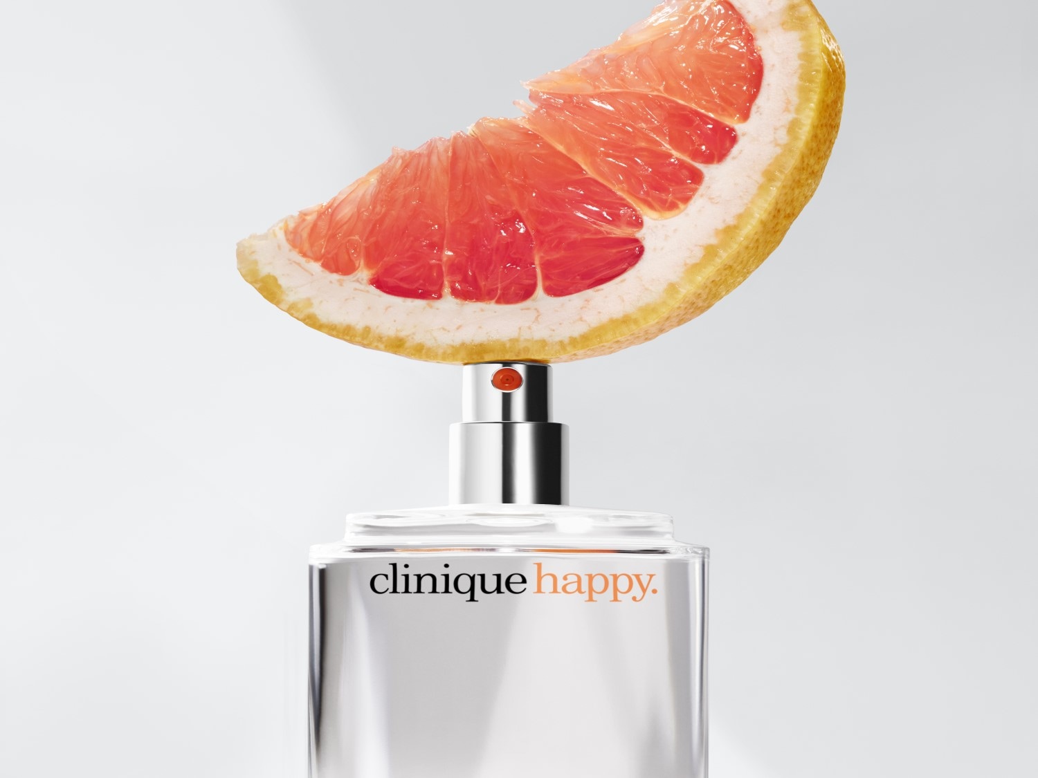Flakon perfum Clinique Happy z srebrną nakrętką, na której umieszczono plasterek różowego grejpfruta, co podkreśla cytrusowy zapach.