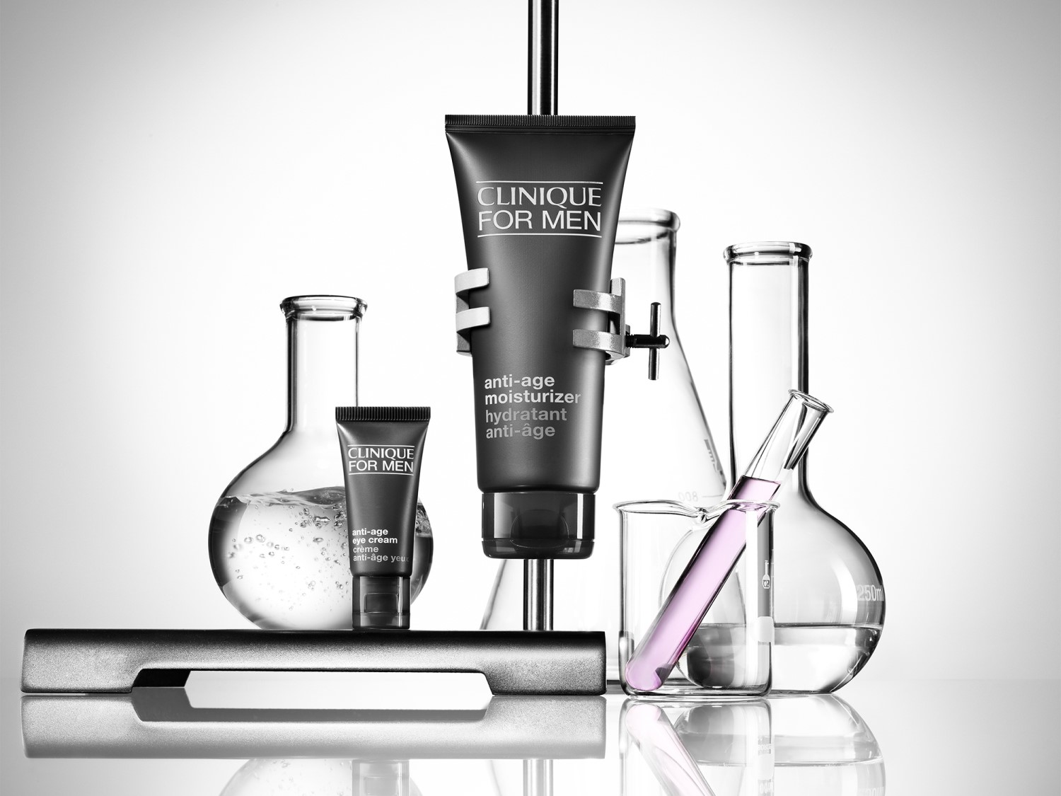 Krem nawilżający i krem pod oczy Clinique For Men anti-age w czarnych tubkach, otoczone laboratoryjnym szkłem, prezentują naukowe podejście do pielęgnacji męskiej skóry.