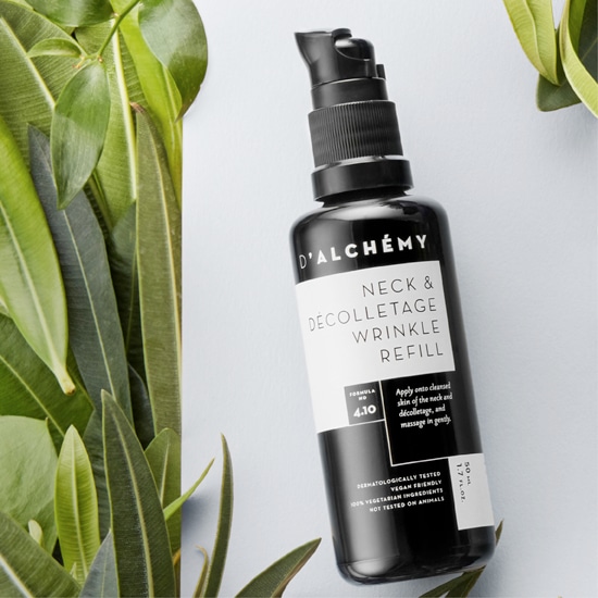 Czarna butelka D'ALCHEMY Neck & Decolletage Wrinkle Refill z pompką, otoczona zielonymi liśćmi, zawiera formułę 4.10 do pielęgnacji szyi i dekoltu, testowana dermatologicznie, wegańska i nietestowana na zwierzętach.