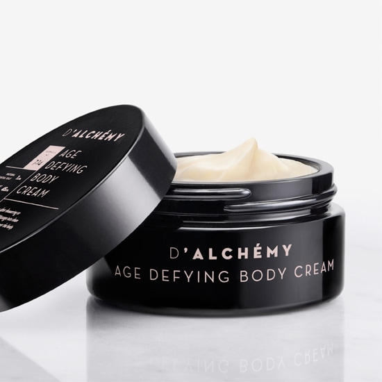 Odkryj D'ALCHÉMY Age Defying Body Cream w czarnym słoiczku z kremową zawartością, który obiecuje odmłodzenie i nawilżenie Twojej skóry.