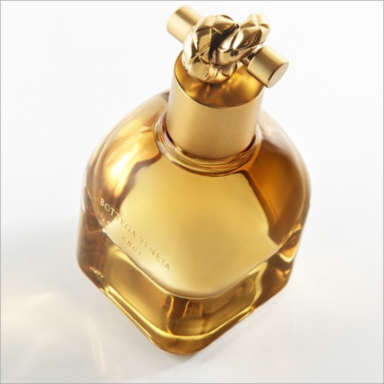 Bursztynowy flakon perfum Bottega Veneta Knot z korkiem w kształcie złotego węzła, emanujący luksusem i wyrafinowaniem.