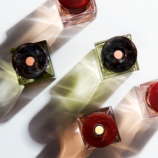 Na białym tle znajdują się flakony perfum w kwadratowych butelkach z okrągłymi korkami w odcieniach czerwieni i zieleni, tworząc elegancką kompozycję.