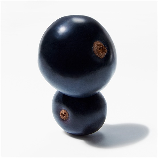 Dwie ciemne jagody ułożone jedna na drugiej na białym tle, tworzące minimalistyczną kompozycję.