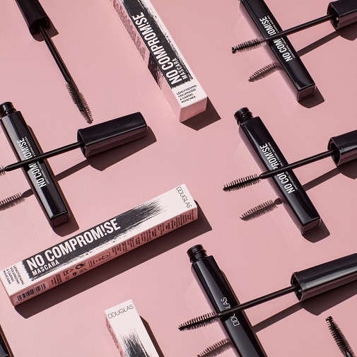 Czarny tusz do rzęs Douglas No Compromise Mascara, wydłużający, zwiększający objętość i pielęgnujący rzęsy, leży na różowym tle obok pudełka.
