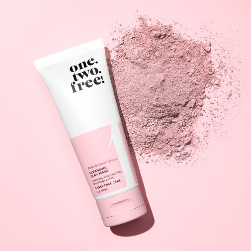 Biało-różowa tuba maski oczyszczającej one.two.free! Cleansing Clay Mask leży na różowym tle obok rozsypanego, różowego proszku.