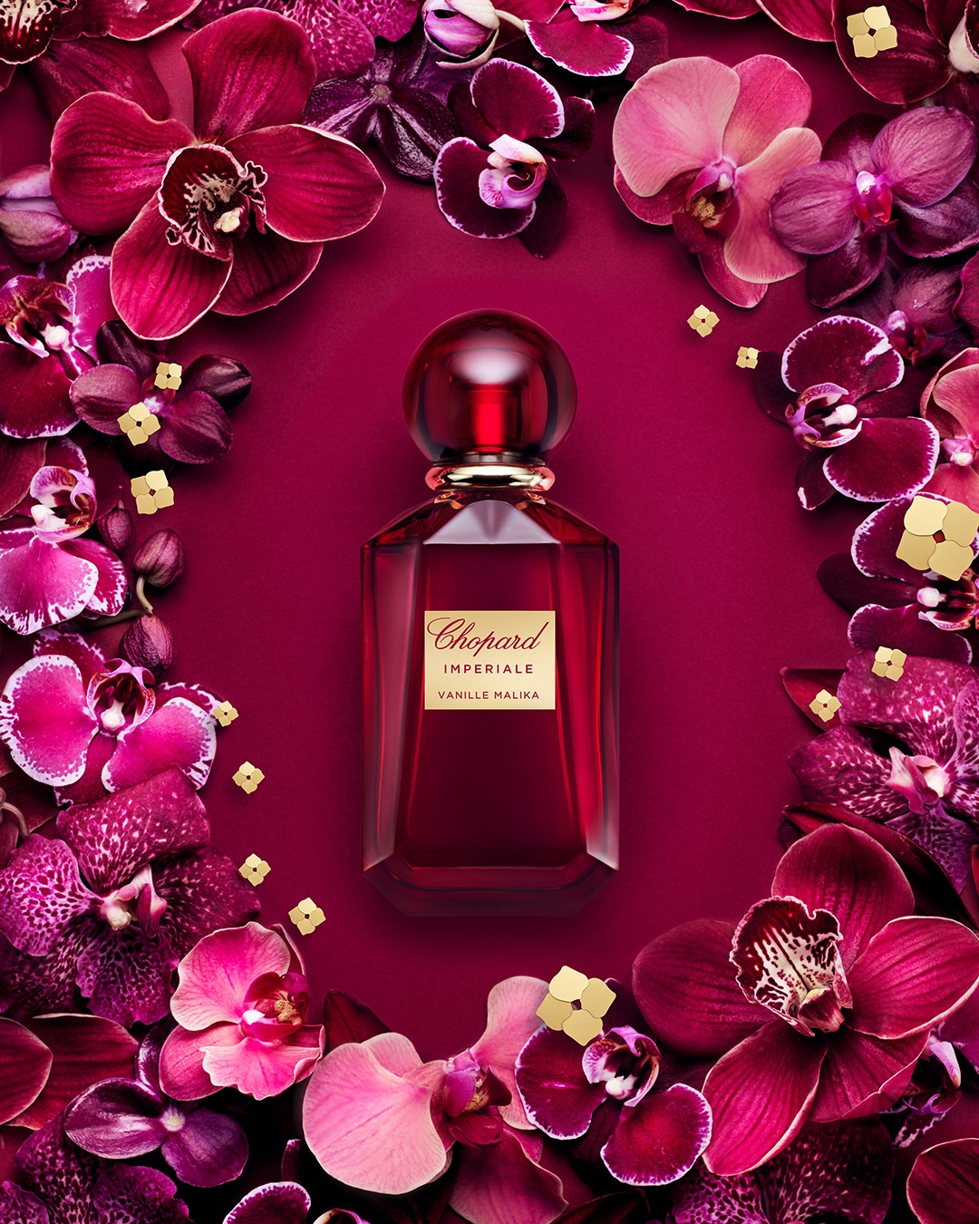 Flakon perfum Chopard Imperiale Vanille Malika w odcieniach czerwieni, otoczony fioletowymi kwiatami orchidei i złotymi akcentami na bordowym tle.