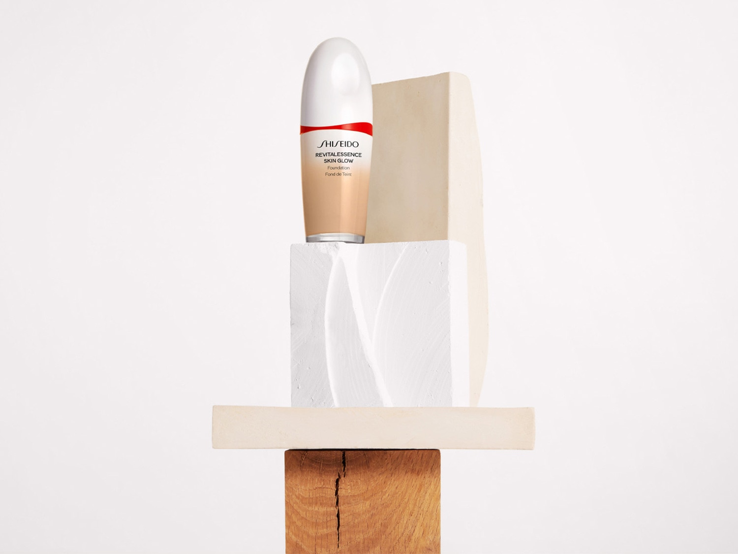 De Shiseido Revitalessence Skin Glow Foundation in een beige fles met een witte dop, gepresenteerd op een stapel houten en witte blokken.