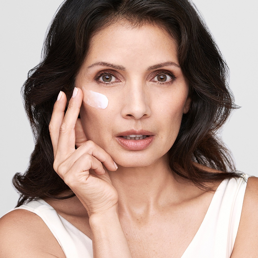 Une femme applique une crème blanche sur sa joue, soulignant l'importance des soins de la peau pour une peau éclatante.