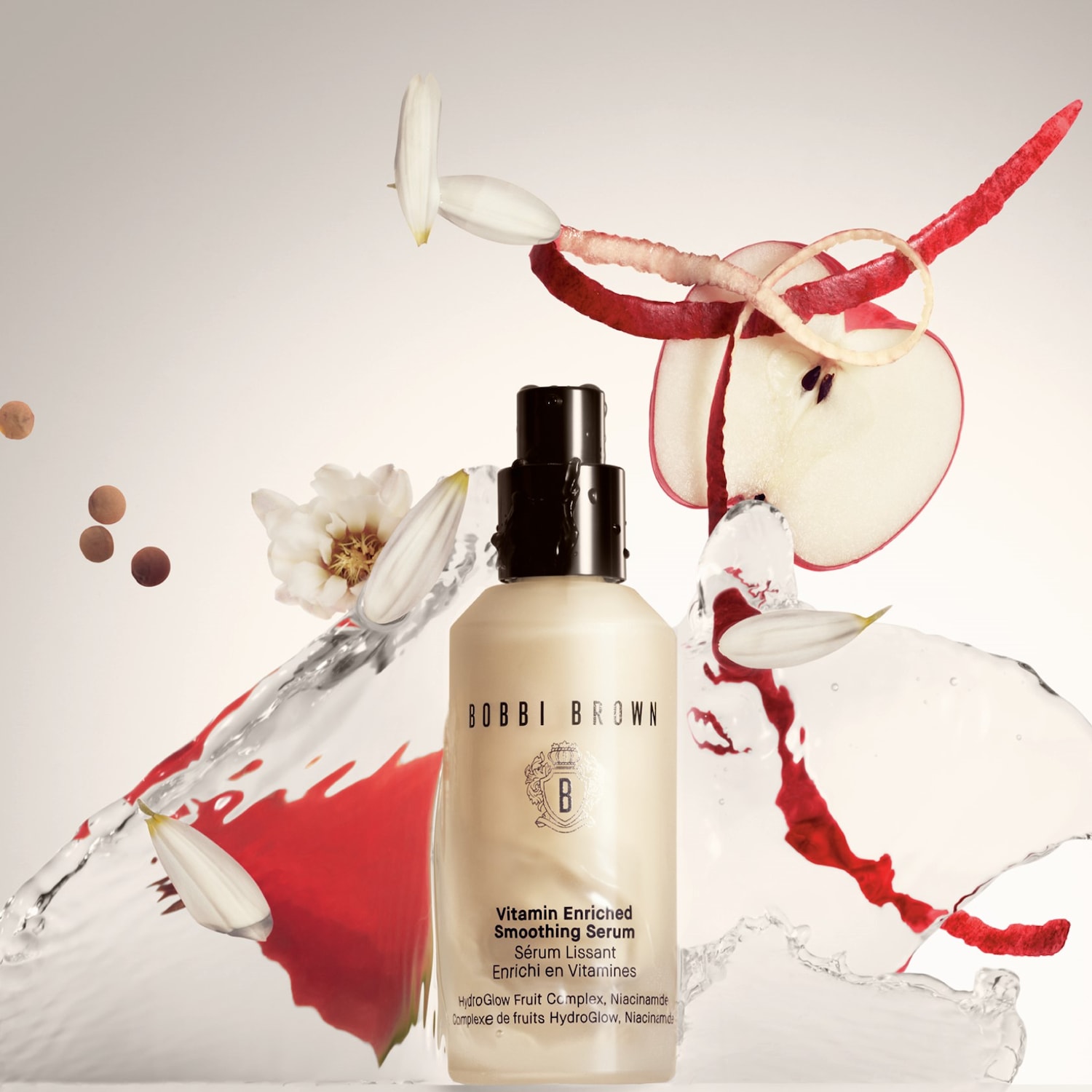 A Bobbi Brown Vitamin Enriched Smoothing Serum bézs színű üvegben, fekete kupakkal, virágokkal, almaszeletekkel és vízcseppekkel körülvéve.