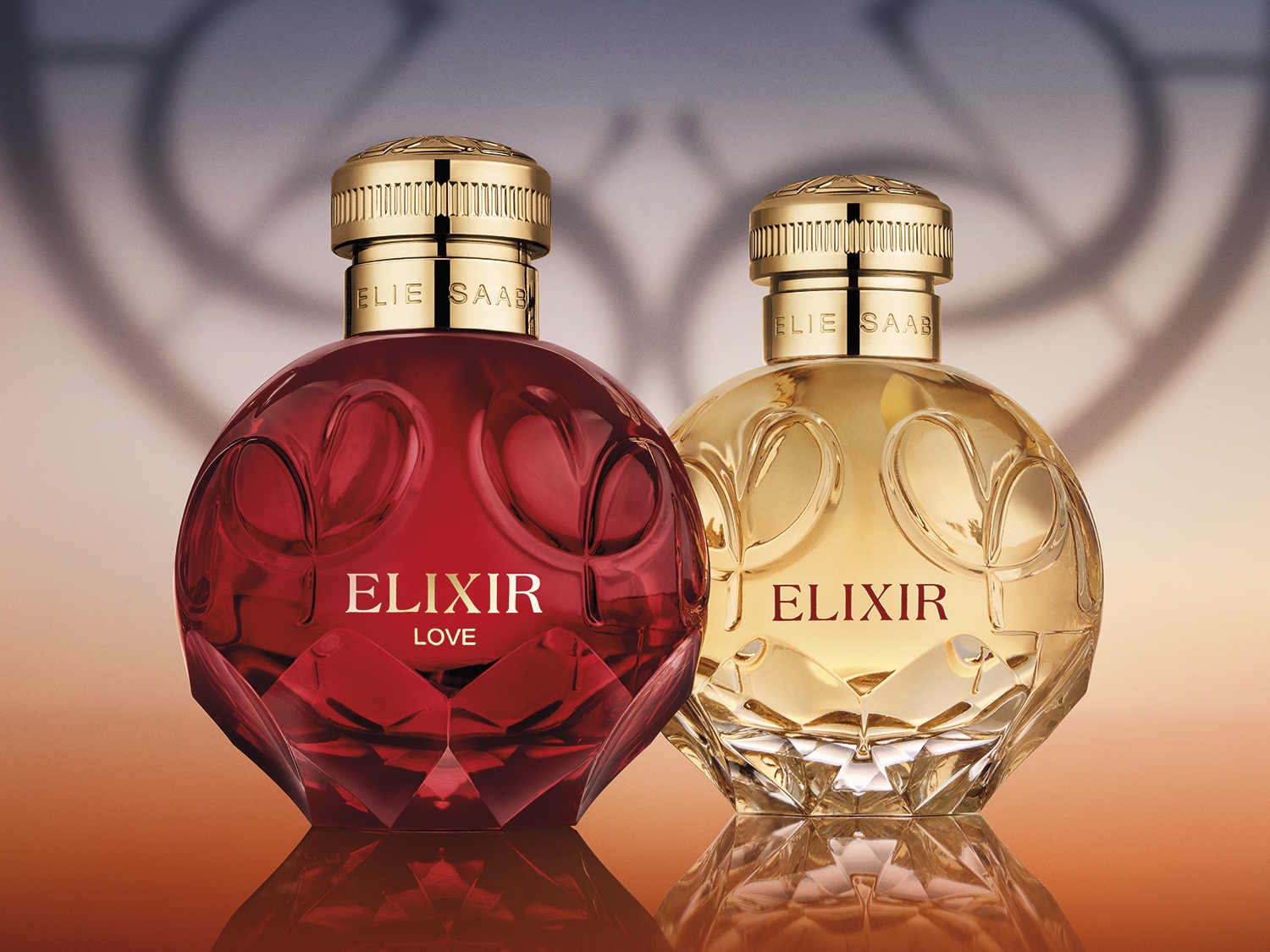 Dwa flakony perfum Elie Saab Elixir: jeden w rubinowej czerwieni z napisem LOVE, drugi złoty, oba z fasetowanymi podstawami i złotymi korkami.