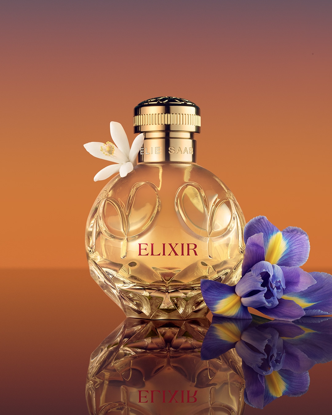 Butelka perfum Elie Saab Elixir o pojemności 50 ml ma okrągły kształt, złotą nakrętkę i jest ozdobiona białymi i fioletowymi kwiatami na złotym tle.