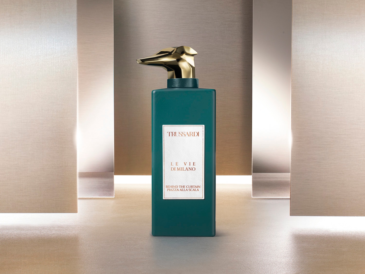 Butelka perfum Trussardi Le Vie Di Milano w kolorze ciemnej zieleni z złotą nakrętką w kształcie głowy psa, na której widnieje biała etykieta z brązowym napisem.