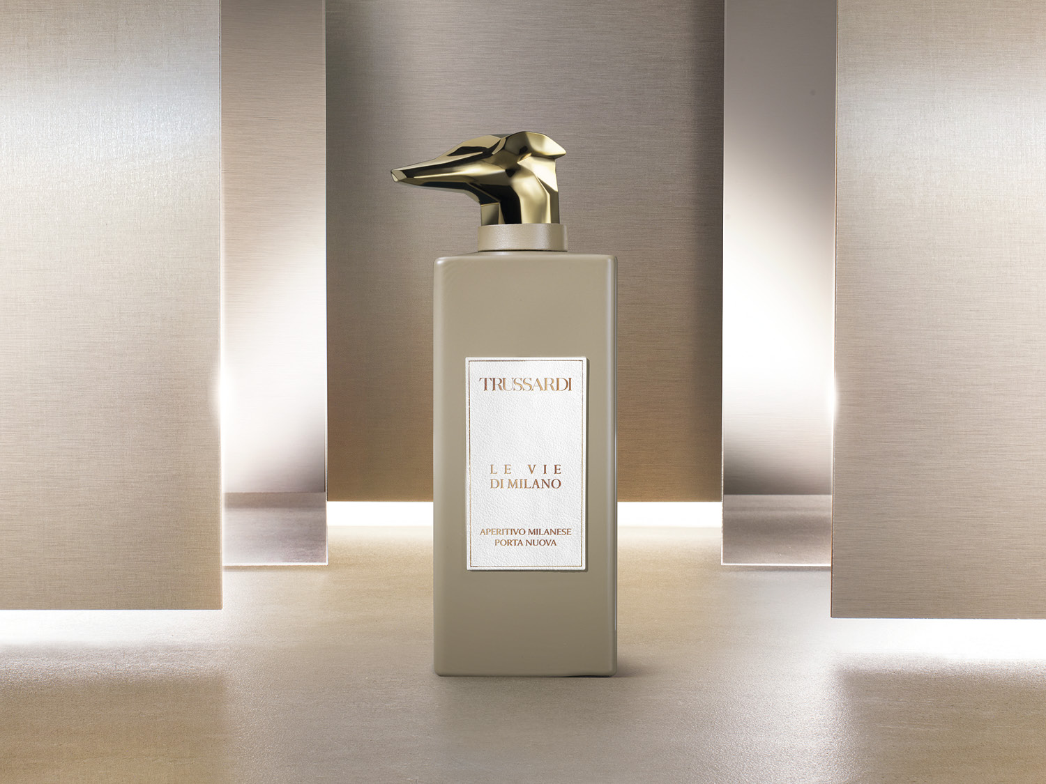 Butelka perfum Trussardi Le Vie di Milano Aperitivo Milanese Porta Nuova ma beżowy, prostokątny flakon z złotą nakrętką w kształcie głowy charta.