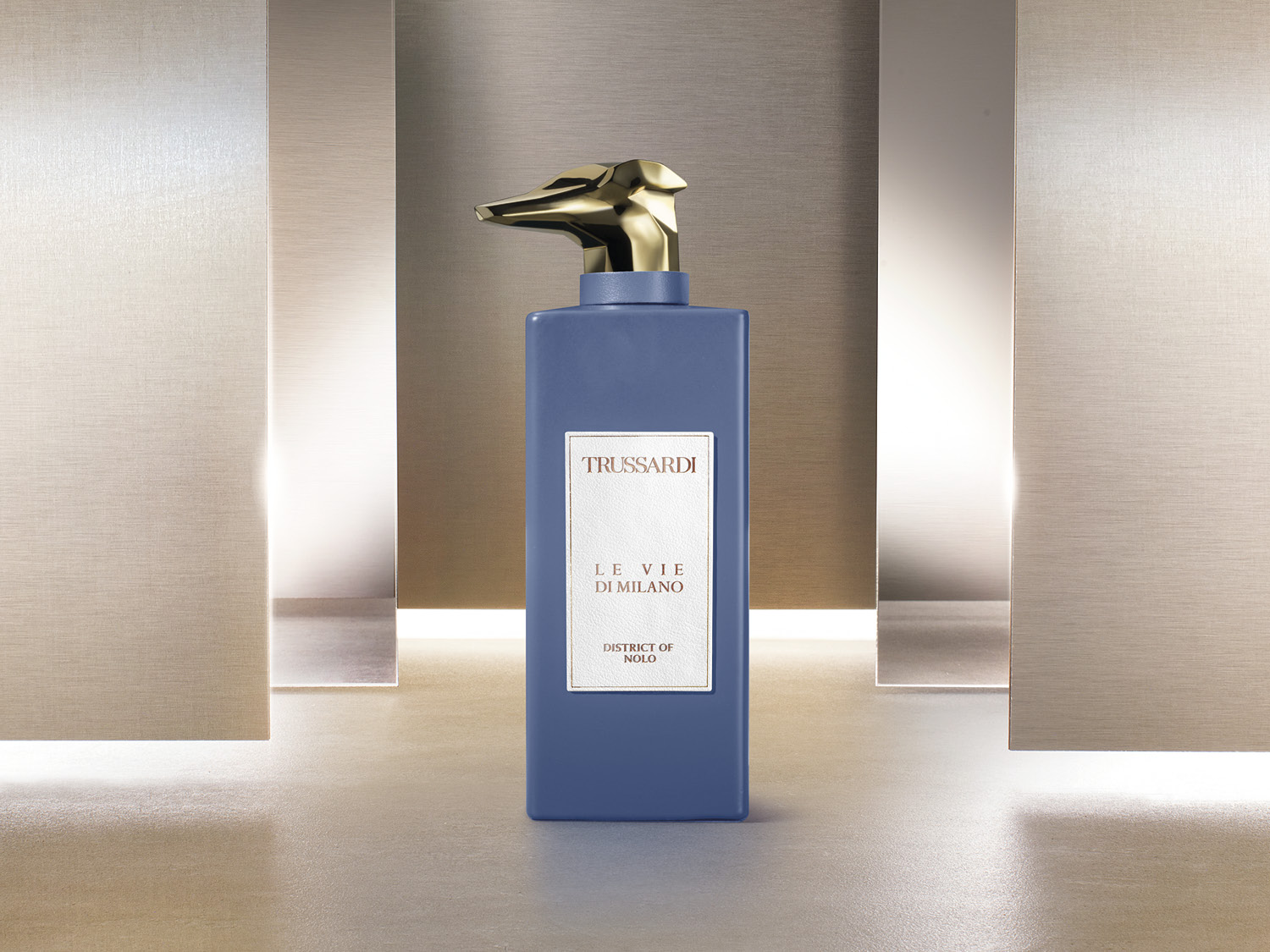Niebieski flakon Trussardi Le Vie Di Milano District of Nolo z złotą nakrętką w kształcie głowy charta, na etykiecie nazwa perfum.