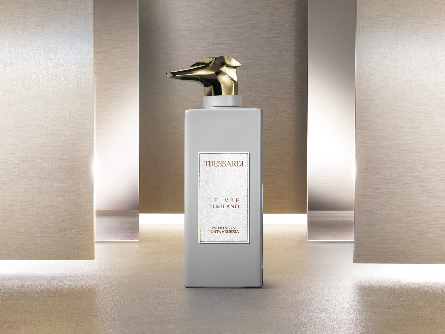 Szary flakon perfum Trussardi Le Vie Di Milano Walking in Porta Venezia z złotą nakrętką w kształcie głowy psa.