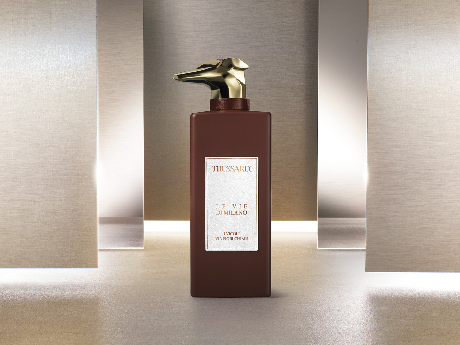 Brązowa butelka perfum Trussardi Le Vie Di Milano I Vicoli Via Fiori Chiari z złotą nakrętką w kształcie głowy psa.