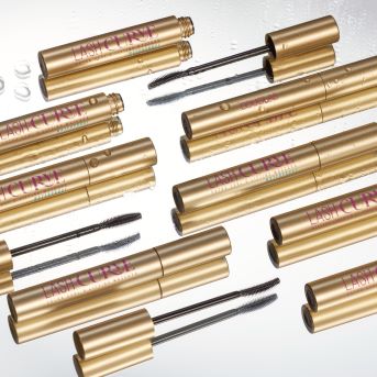 Primo piano di mascara Lash Cure dorati con applicatori neri su una superficie riflettente, che mostra il design elegante e la funzionalità del prodotto.