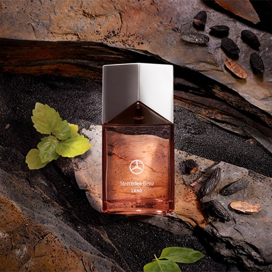 Butelka perfum Mercedes-Benz LAND o pojemności 100 ml na tle kamieni i ziaren tonki.
