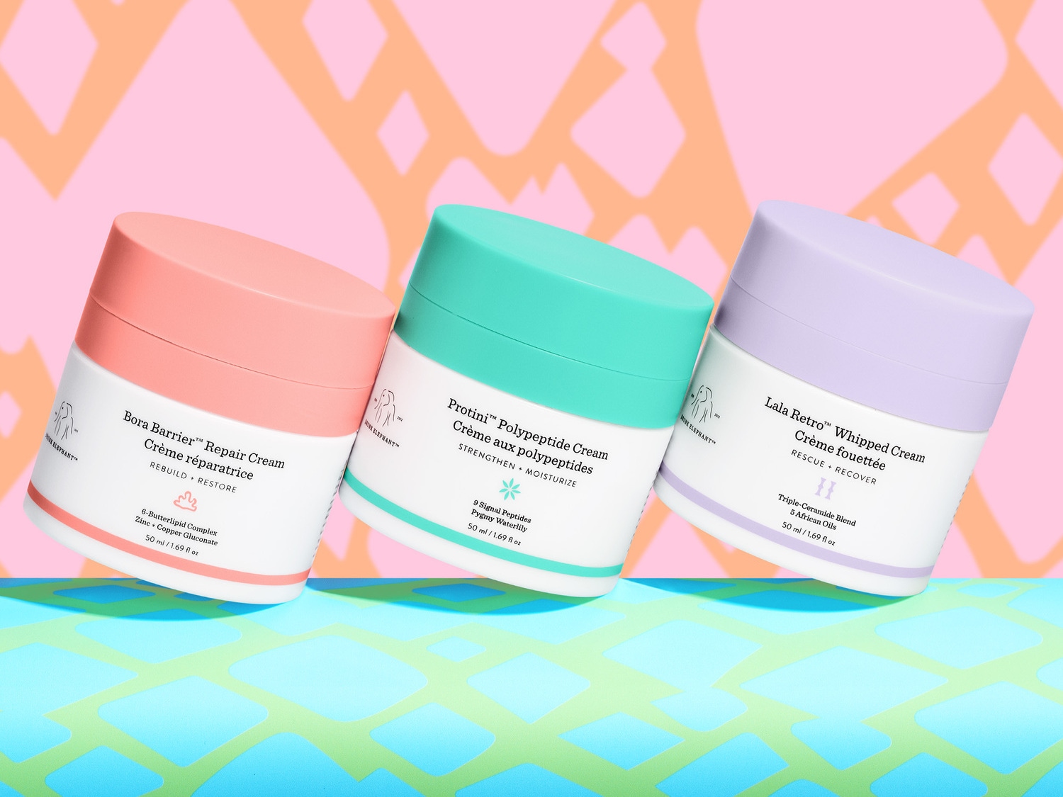 Drie potten Drunk Elephant crème: Bora Barrier Repair Cream met een perzikkleurige deksel, Protini Polypeptide Cream met een turquoise deksel en Lala Retro Whipped Cream met een lila deksel.