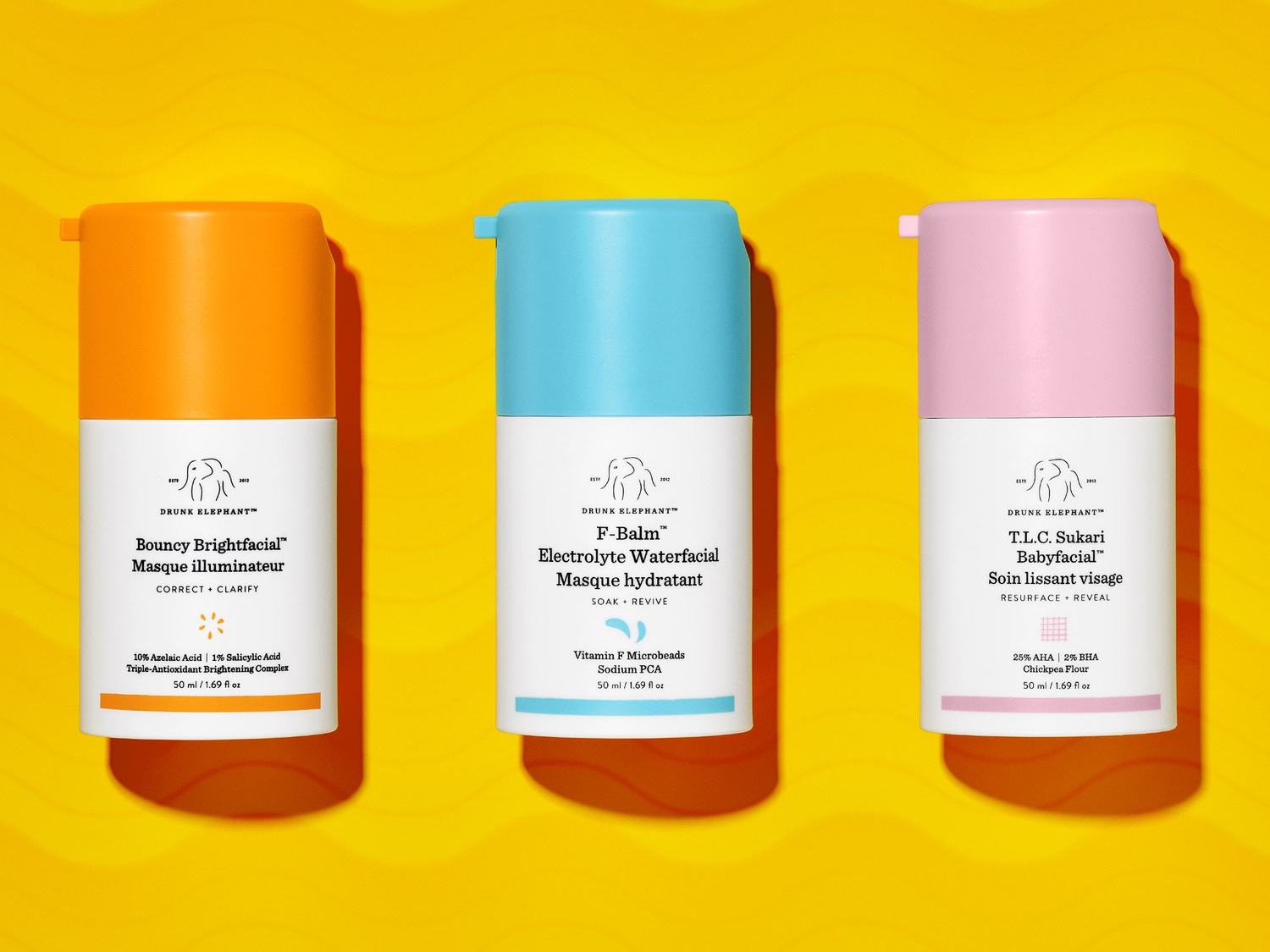 Drie Drunk Elephant maskers in oranje, blauw en roze verpakkingen, elk met een witte basis en de productnaam.
