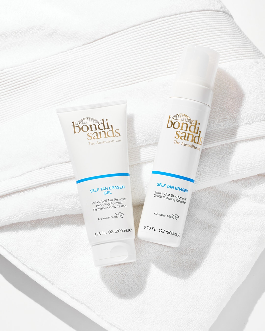Twee witte flessen Bondi Sands Self Tan Eraser, een gel en een zachte schuimende reiniger, liggen op een witte handdoek.