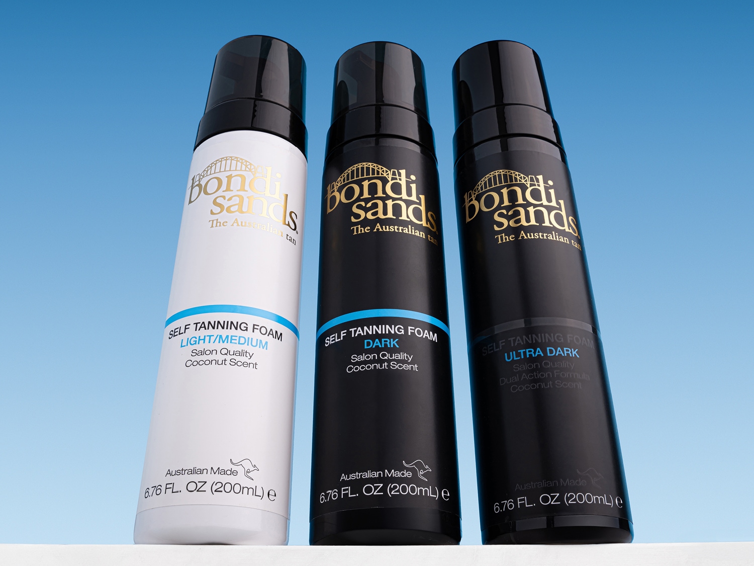 Drie flessen Bondi Sands zelfbruinende mousse, variërend van licht/medium in een witte fles tot donker en ultra donker in zwarte flessen, voor een salonkwaliteit bruine kleur met kokosgeur.