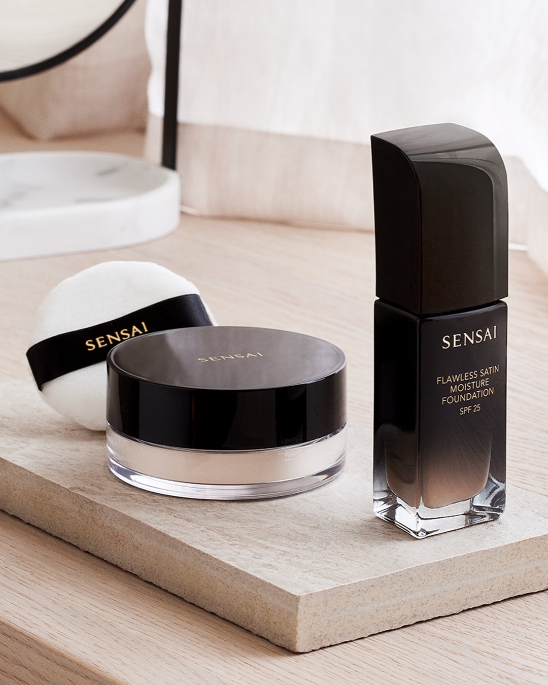 Puder i podkład Sensai Flawless Satin Moisture Foundation SPF 25 w eleganckich, czarnych opakowaniach, zapewniające nieskazitelne wykończenie.