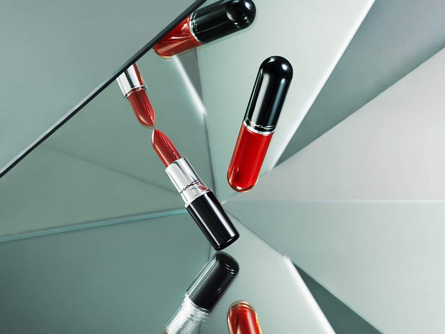 Een rode MAC lippenstift en een rode MAC lipgloss, beide met een zwarte dop, liggen op een spiegelend oppervlak dat hun reflecties toont.