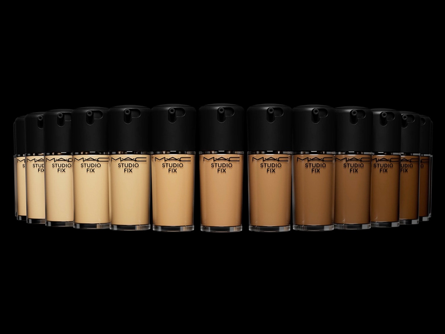 Een reeks MAC Studio Fix foundations in verschillende huidtinten, van licht tot donker, gepresenteerd in glazen flesjes met zwarte doppen, staat op een rij tegen een zwarte achtergrond.
