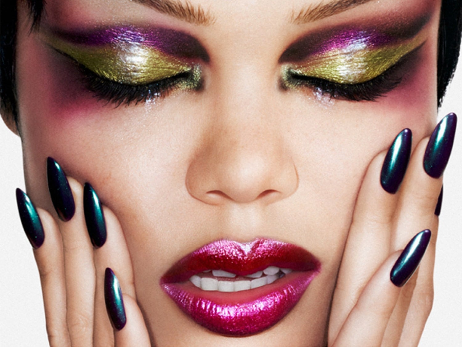 Een close-up van een vrouw met glanzende, metallic oogschaduw in paars en goud, glinsterende roze lippenstift en lange, puntige nagels in een iriserende blauwgroene kleur.