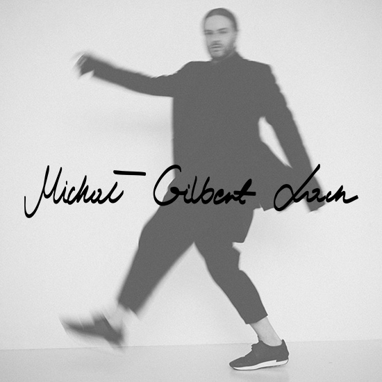 Czarno-białe zdjęcie mężczyzny w płaszczu, w ruchu, z napisem „Michał Gilbert Lach” na pierwszym planie.