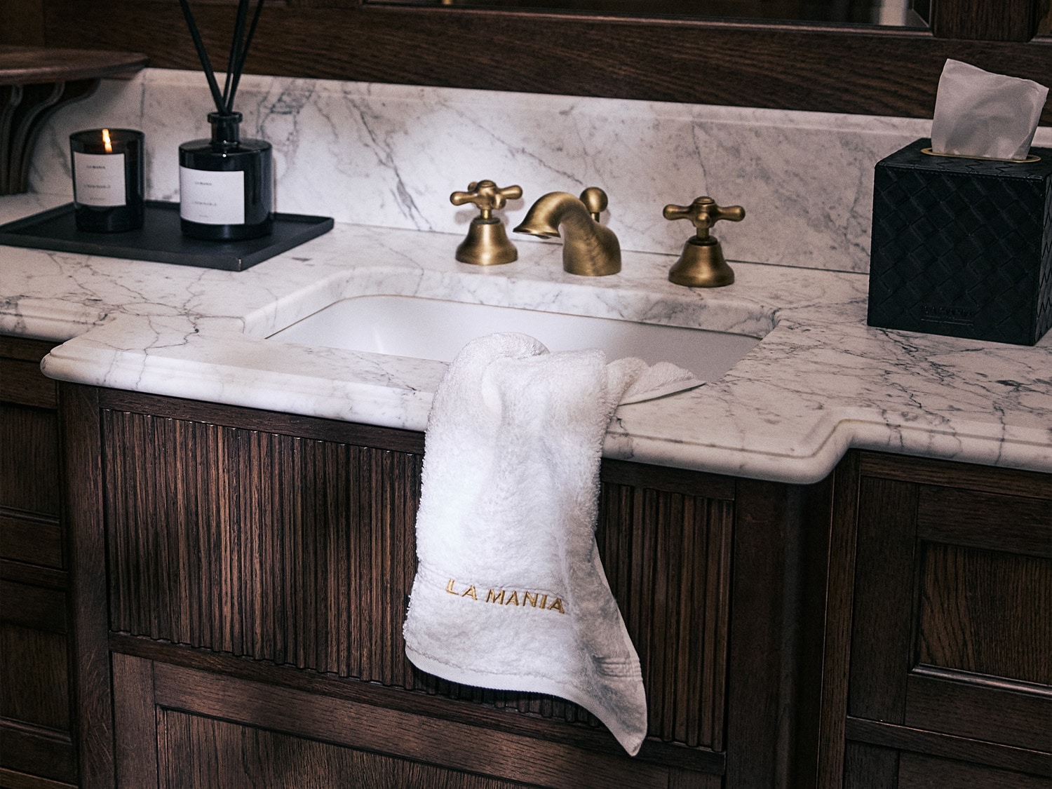 Elegancka łazienka z marmurowym blatem, złotą armaturą i ręcznikiem z napisem LA MANIA, tworząca luksusową atmosferę.