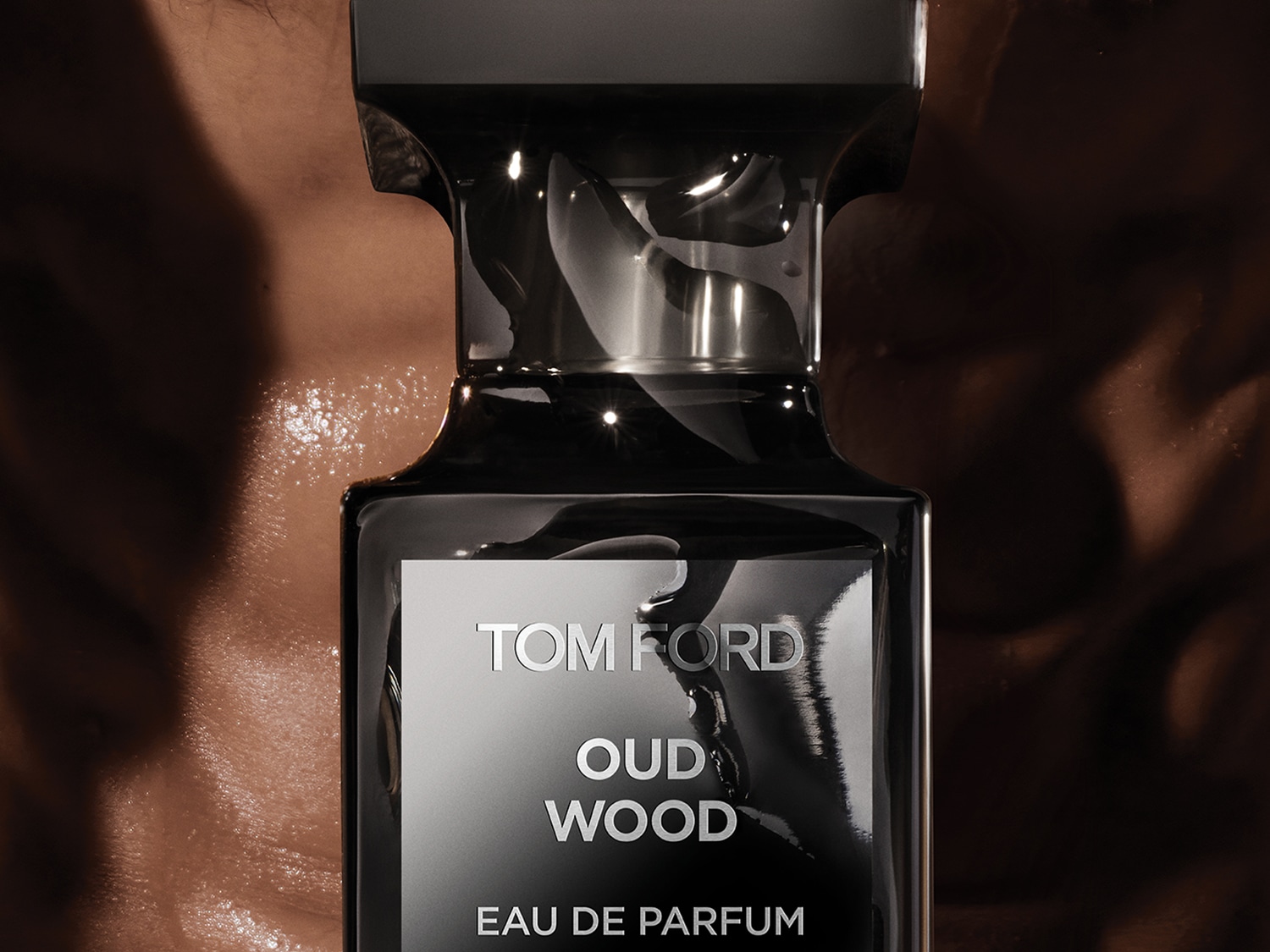 Een close-up van een Tom Ford Oud Wood Eau de Parfum fles, met een glanzende, donkere verpakking en zilveren letters, tegen een bruine achtergrond.