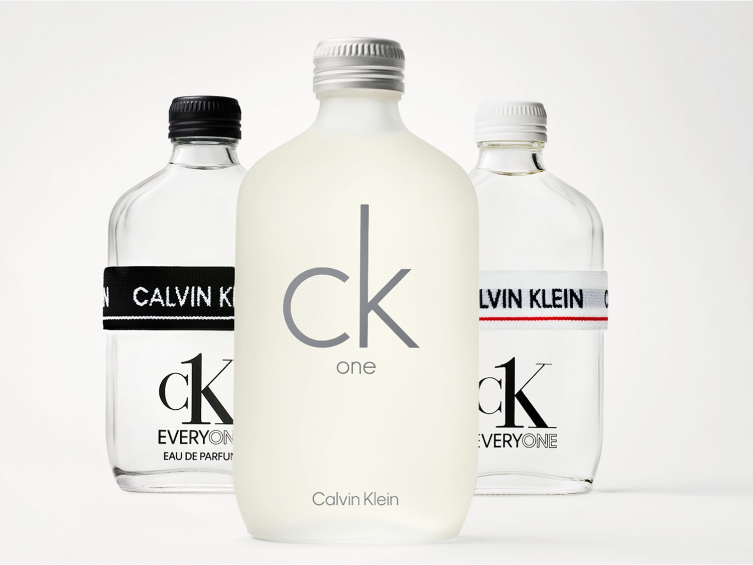 Tři flakony parfémů Calvin Klein CK One a CK Everyone s minimalistickým designem a různými barevnými akcenty.