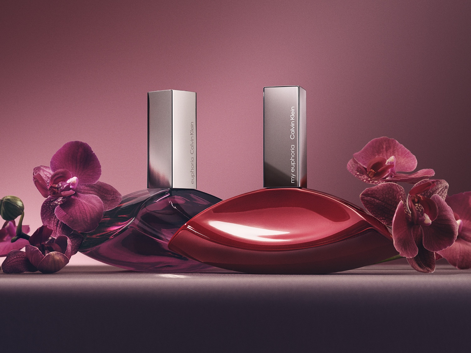 Dva flakony Calvin Klein Euphoria a My Euphoria obklopené purpurovými květy orchidejí, které doplňují jejich elegantní design.