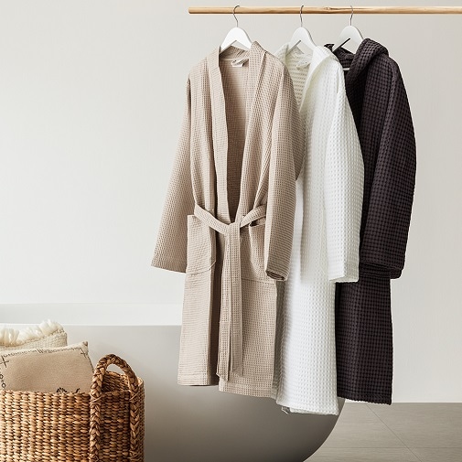 Na wieszaku wiszą trzy szlafroki frotte w kolorach: beżowym, białym i ciemnobrązowym.