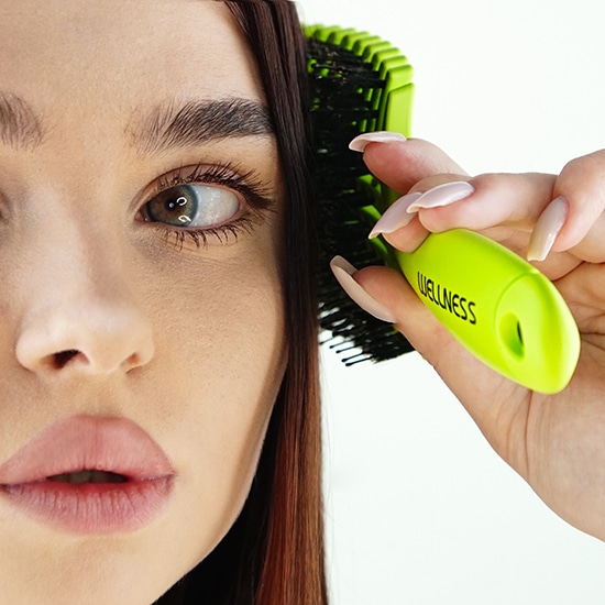 Kobieta czesze włosy jasnozieloną szczotką Wellness, dbając o zdrowie i piękno.