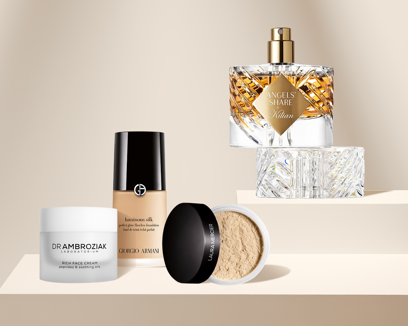 Na zdjęciu znajdują się luksusowe produkty do pielęgnacji skóry i makijażu, w tym krem do twarzy Dr. Ambroziak, podkład Giorgio Armani Luminous Silk, puder Laura Mercier i perfumy Kilian Angels' Share.