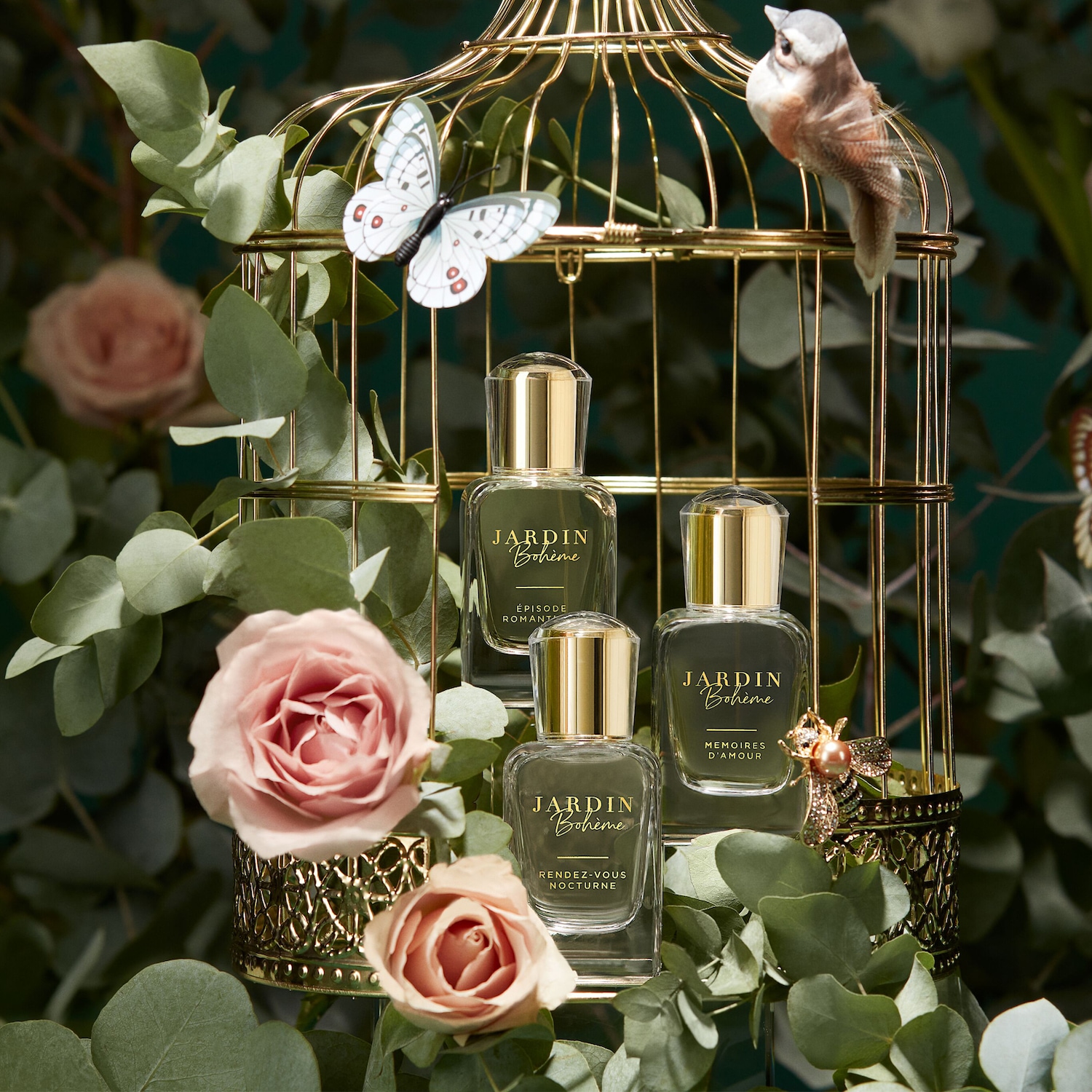 Trzy flakony perfum Jardin Bohème w złotej klatce dla ptaków, ozdobionej różami, motylem i figurką ptaka, tworzą romantyczną kompozycję.