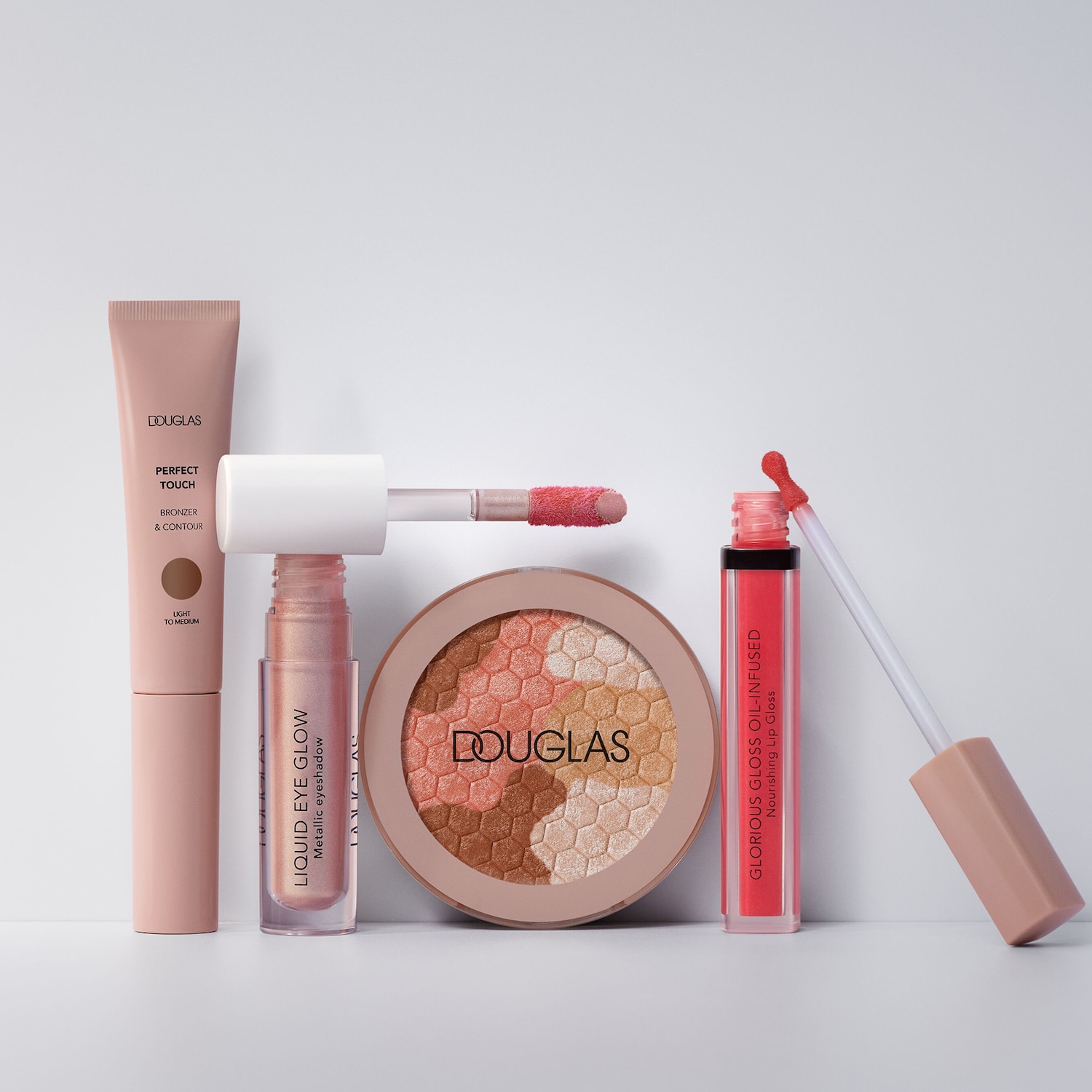 Różnorodność kosmetyków Douglas w odcieniach różu i brązu, w tym bronzer, cień do powiek w płynie, rozświetlacz i błyszczyk do ust, idealne do stworzenia kompletnego makijażu.