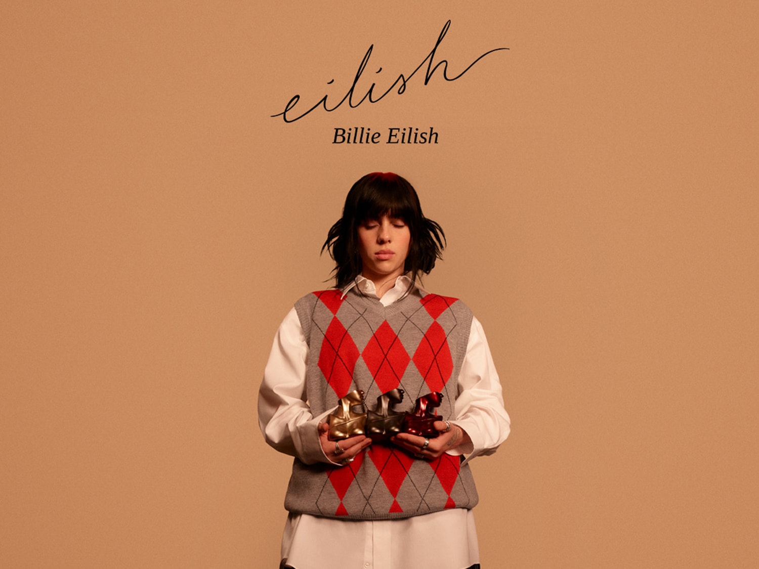 Na beżowym tle Billie Eilish trzyma w dłoniach flakony perfum w kształcie popiersia, ubrana w sweter w romby i białą koszulę, a nad nią widnieje jej imię.