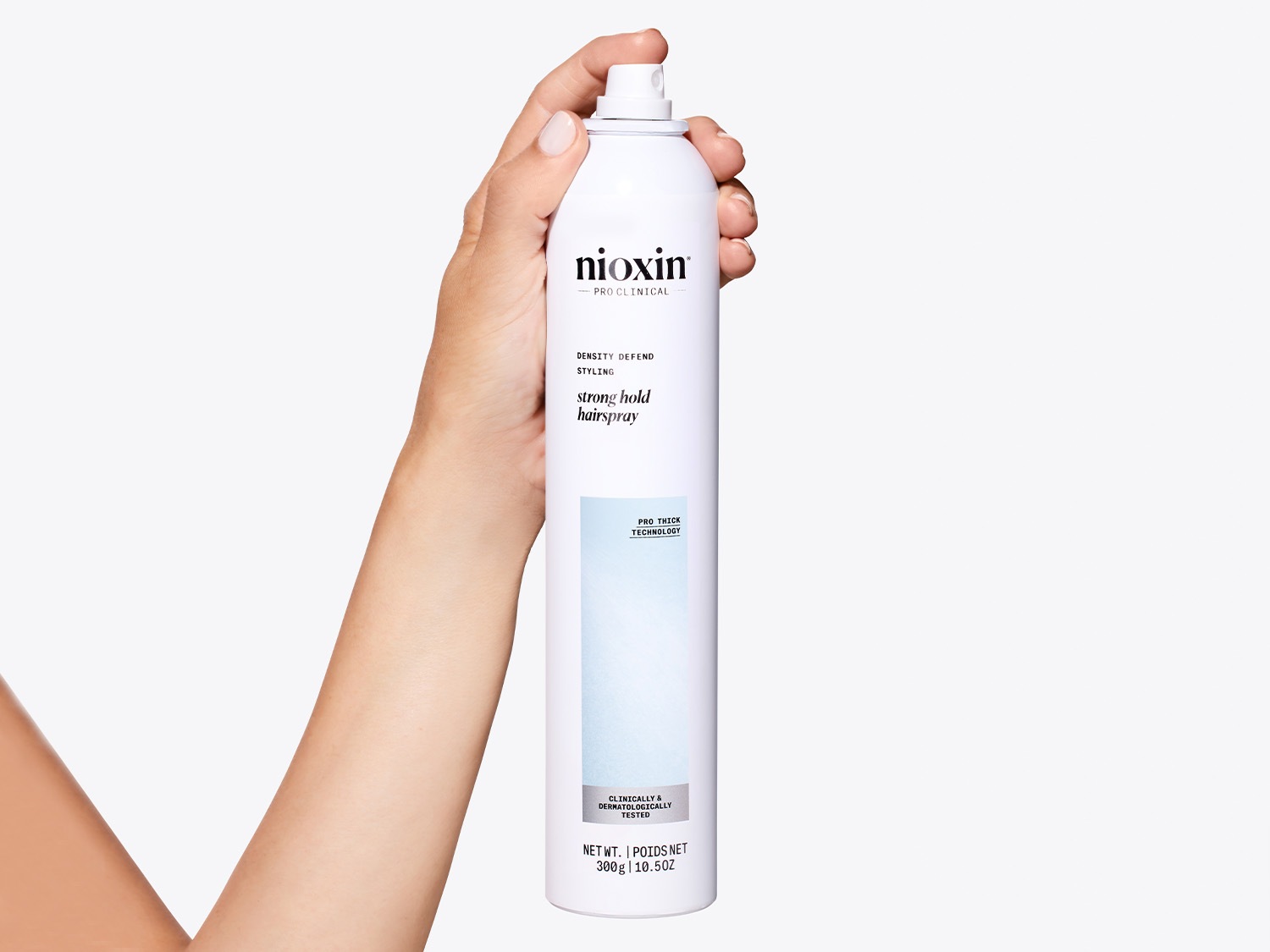 A mão segura um frasco branco de spray de cabelo Nioxin Pro Clinical Strong Hold, destacando sua fórmula de defesa da densidade e tecnologia pró-espessa para fixação forte.