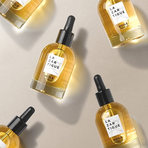 Prezentacja olejku do włosów La Zarigue w przezroczystej butelce z czarną pipetą, etykieta z nazwą marki i napisem „Huile des rêves”.