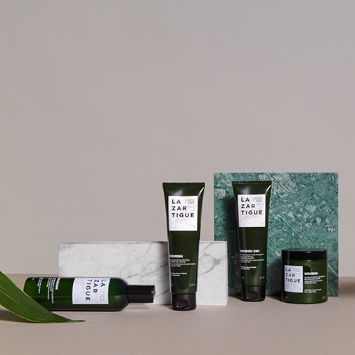 Na beżowym tle znajdują się produkty do pielęgnacji włosów marki Lazartigue w ciemnozielonych opakowaniach z białymi etykietami, w tym butelka, tubki i słoiczek.