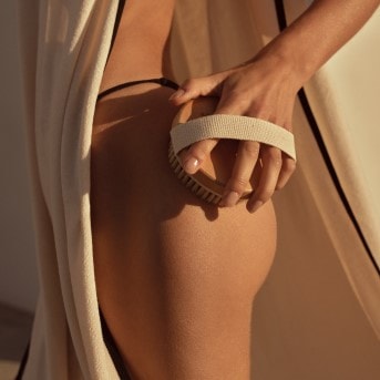 Nahaufnahme einer Frau, die eine Trockenbürste auf ihrer Haut anwendet, um abgestorbene Hautzellen zu entfernen und die Durchblutung zu fördern.