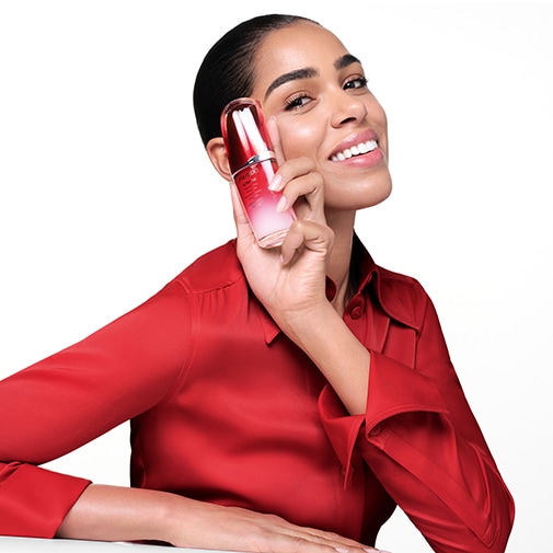 Eine Frau mit einem roten Hemd hält eine Shiseido Eudermine Flasche in der Hand, die eine Mischung aus roter und weißer Flüssigkeit enthält.