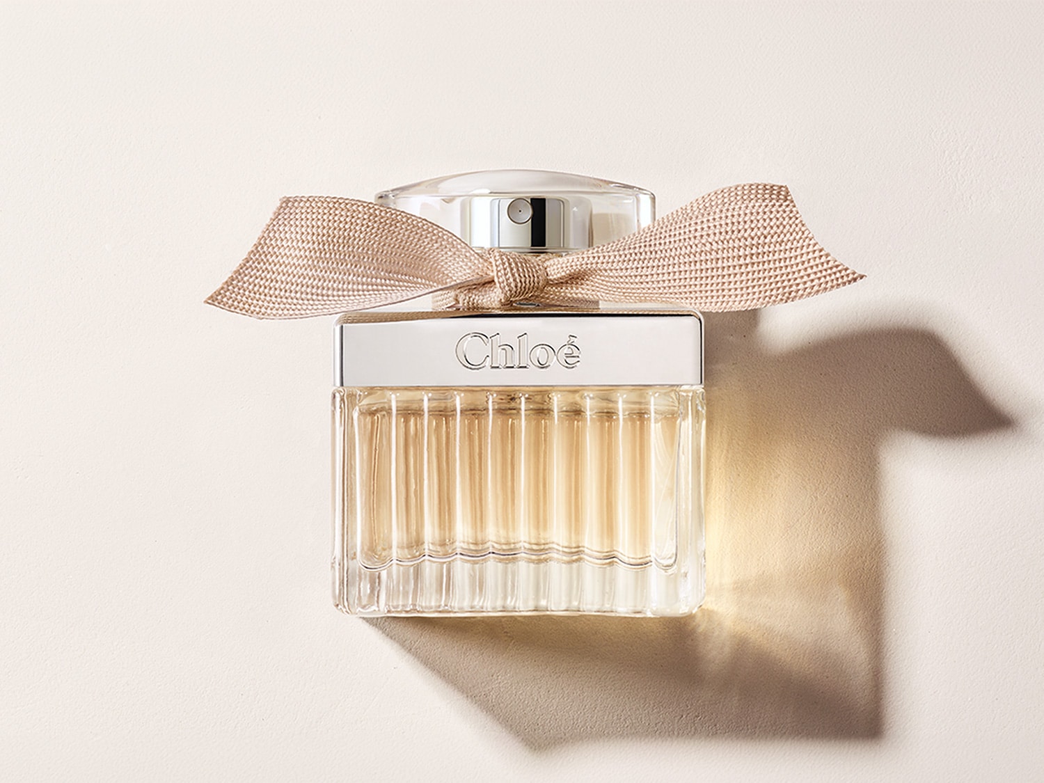 Butelka perfum Chloé z beżową kokardką, przezroczystym szkłem i srebrnym korkiem emanuje elegancją i subtelnym urokiem.