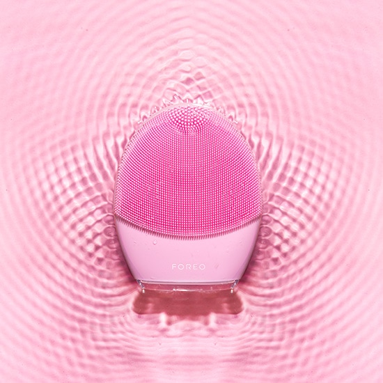 Różowa silikonowa szczoteczka do twarzy Foreo na tle wody, idealna do codziennej pielęgnacji skóry.