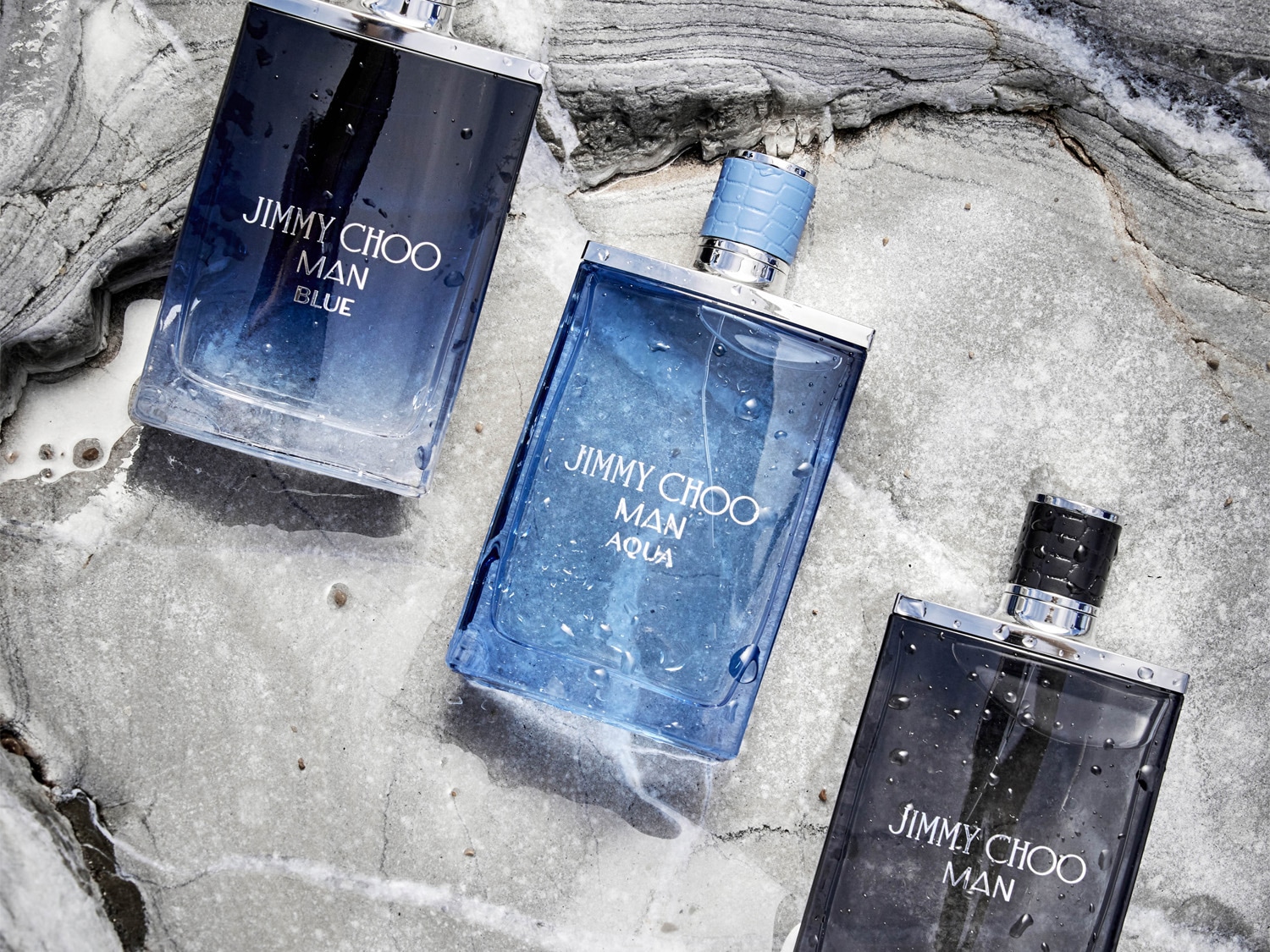 Drie flessen Jimmy Choo herenparfum, waaronder Man Blue, Man Aqua en Man, liggen op een grijze stenen achtergrond met waterdruppels.